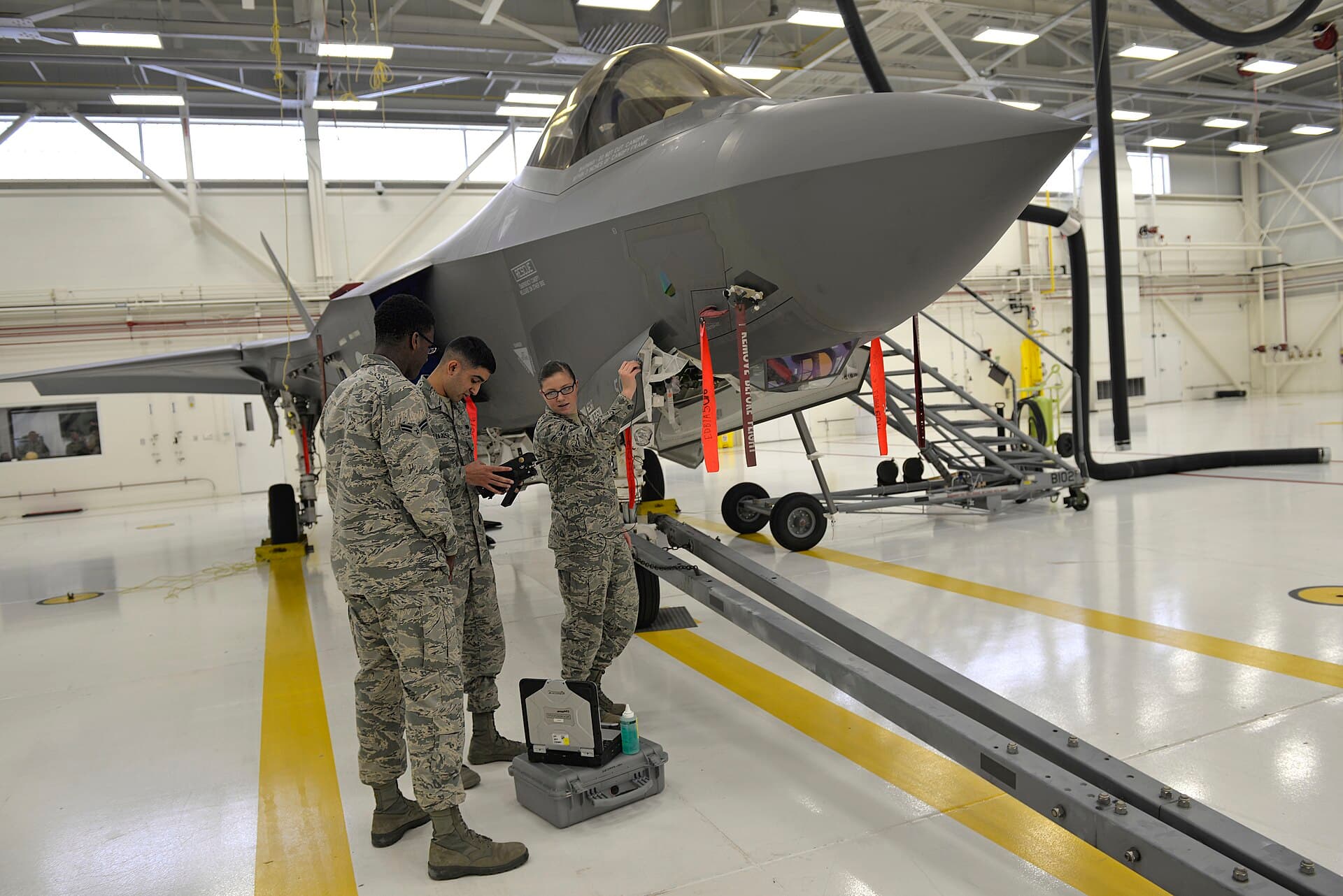 Technicians with inspection equipment beside a jet in a maintenance hangar
